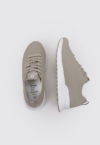 Zapatillas de punto beige con un upper texturizado, suela de goma blanca y una lengüeta. El interior presenta texto impreso y etiqueta de talla. Diseño casual.