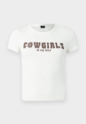 Fehér pamut póló kerek nyakkal és rövid ujjakkal. Ki van fejezve feltűnő barna szöveggel, ami azt mondja: "COWGIRLS IN THE WILD." Általános szabású.