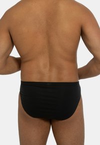Costumi da bagno neri, realizzati in materiale liscio ed elastico, caratterizzati da un design semplice e una vestibilità aderente, mostrati da dietro.