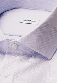Primo piano di un colletto e bottoni di una camicia a righe a spina di pesce di colore viola chiaro, con un'etichetta "seidensticker" all'interno del colletto.