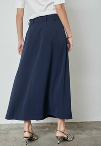 Falda midi azul marino plisada con textura suave, cintura alta y aberturas laterales. Combinada con zapatos de tacón beige con estampado de piel de serpiente.