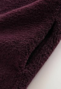 Plüschstoff in tiefem Lila, mit einer weichen, strukturierten Oberfläche und einem leicht flauschigen Aussehen sowie subtiler Ausstrahlung, übereinander gefaltet.