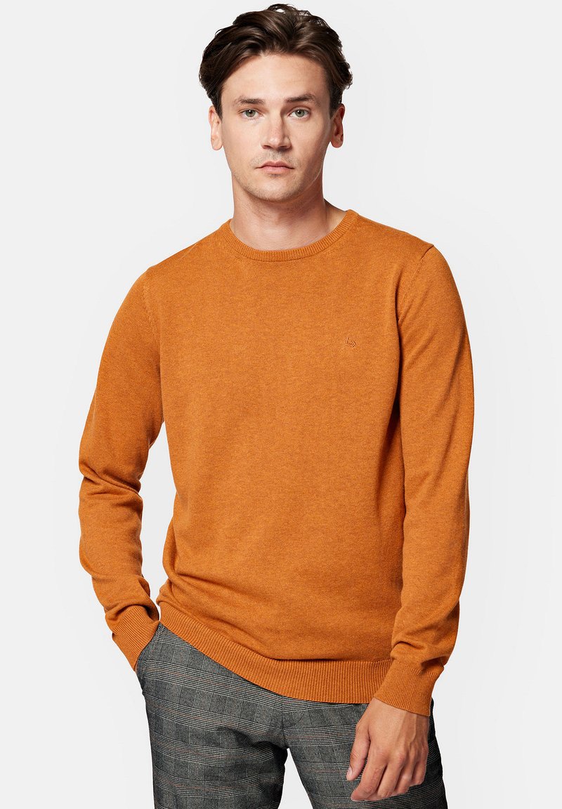 Pomarańczowy sweter z okrągłym dekoltem, wykonany z miękkiego dzianinowego materiału, z długimi rękawami i ściągaczami na mankietach, w połączeniu z spodniami w kratę.