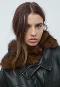 Giacca di pelle nera con colletto in pelliccia marrone, dotata di una zipper diagonale e dettagli testurizzati sul colletto e sul rever.