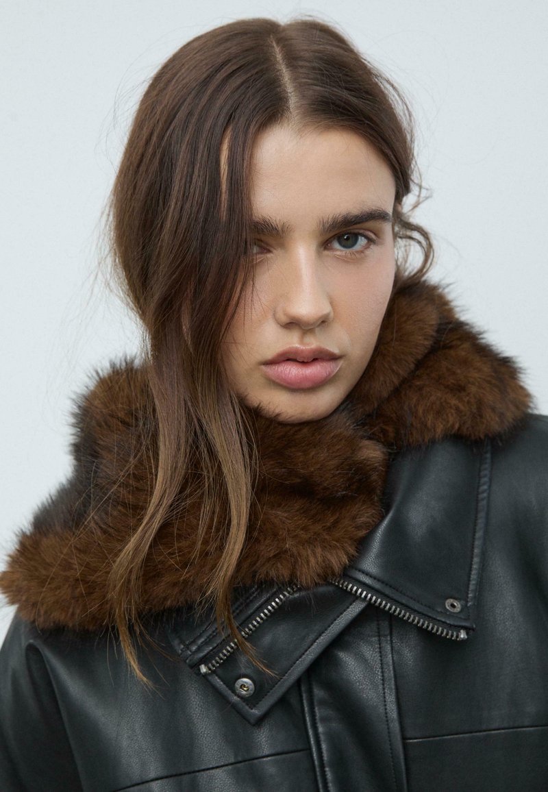 Giacca di pelle nera con colletto in pelliccia marrone, dotata di una zipper diagonale e dettagli testurizzati sul colletto e sul rever.