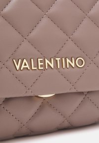 Quiltad taupe läderyta med guldmetalliska "VALENTINO"-logotypbokstäver centrerade på en vikbar flik.