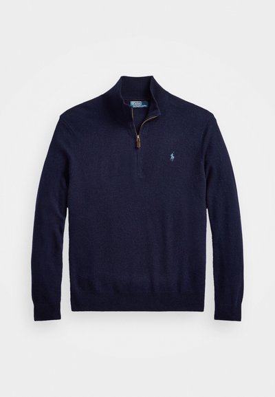 Marineblå hettegenser med glidelås i en myk tekstur, med ribbestrikket krage og mansjetter. Har en liten brodert logo på venstre bryst.