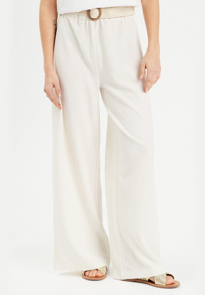 Pantalons à jambes larges en crème avec un tissu texturé, une ceinture tressée avec une boucle ronde, associés à des sandales plates.