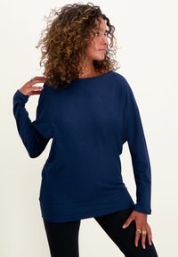 Marineblaues, langärmeliges Oberteil mit lockerer Passform und weitem Ausschnitt. Weicher Stoff mit glatter Textur. Kombiniert mit schwarzen Hosen.