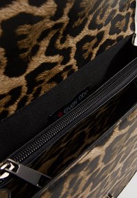 Torebka w panterkę z teksturowaną, futerkową powierzchnią, czarnym wnętrzem, zamknięciem na suwak i metką z logo. Kompaktowy i usztywniony design.
