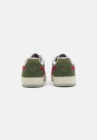 Green and burgundy sneakers with suede and textile materials, featuring a cream sole and notable logo detail on the heel.