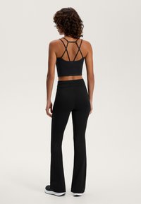 Čierny športový crop top s prekríženými ramienkami a zodpovedajúcimi rozšírenými nohavicami. Hladká textura, elegantný dizajn a prispôsobený na pohodlie a pohyb.