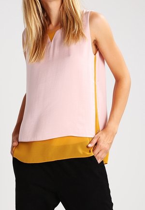 Mouwloos topje met een lichtroze buitenlaag en een v-hals, en een gele binnenlaag. De randen zijn recht, met zijsplitten voor meer bewegingsvrijheid.