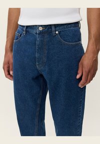 Dunkelblaue Jeans aus Denim mit klassischem Schnitt, ausgestattet mit Fronttaschen, einem Knopfverschluss und kontrastierenden Steppnähten.
