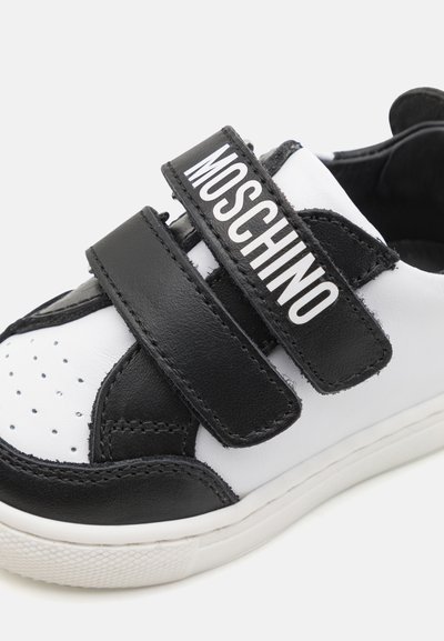 Sneaker bianco e nero realizzato in pelle sintetica, con punta perforata, cinturini in velcro regolabili e suola in gomma testurizzata.