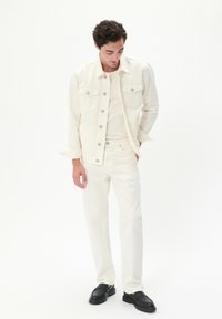 Chaqueta de mezclilla blanca y pantalones a juego con una camisa blanca ajustada. Mocasines negros. El conjunto presenta detalles de botones y un diseño limpio.