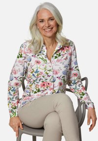 Langärmliges Hemd mit Knopfleiste in weißer Grundfarbe, verziert mit einem bunten Blumen- und Schmetterlingsdruck in Rosa, Blau und Grün.