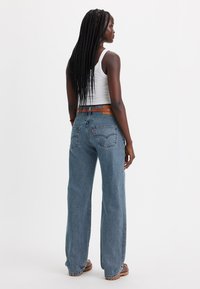 Lichtblauwe wijde jeans met een hoge taille, denimstof en zichtbare achterzakken. Gecombineerd met een witte tanktop en een bruine riem.