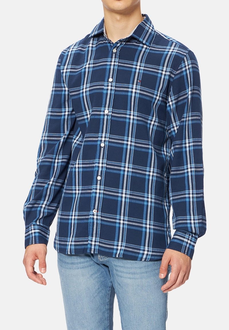 Chemise à carreaux bleue avec col boutonné, manches longues et poche poitrine. Fabriquée en coton avec une texture lisse et des motifs contrastés.