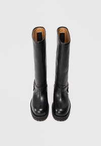 Botas altas de cuero negro con punta redonda, suelas gruesas y correas de hebilla laterales, mostradas de pie sobre un fondo blanco.