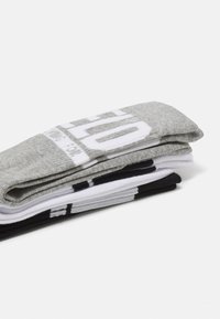 Tres pares de calcetines apilados: grises con texto blanco, blancos con detalles negros y negros con una raya blanca. Mezcla de algodón, textura sutil.
