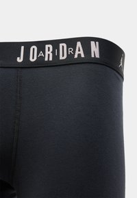 Μαύρο αθλητικό σορτς με λεία υφή και φαρδιά μέση πο�υ φέρει τη λέξη "JORDAN" και το λογότυπο Jumpman σε γκρι χρώμα.