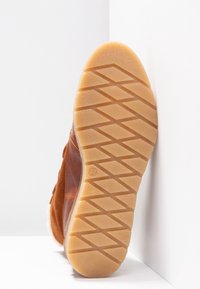 Bota de ante marrón con una suela de goma texturizada. La suela presenta un patrón en zigzag para mayor agarre, y el interior está forrado con un material suave.