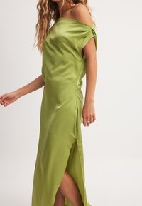 Žalias satino su pūstomis rankovėmis suknelė be pečių, su šonine skeltuku ir lygiu paviršiumi, sklandžiai krentanti per kūną.