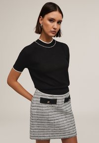 Pull en tricot noir à manches courtes, rehaussé d'une bordure blanche. Associé à une mini-jupe rayée avec des patches noirs et des accents dorés.