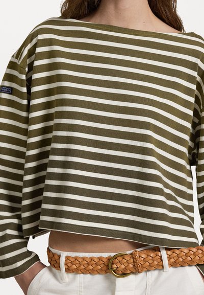 Olivengrønn og hvitstripet langermet topp med off-shoulder hals, kombinert med et flettet brunt lærbelte over høy-midje hvite bukser.