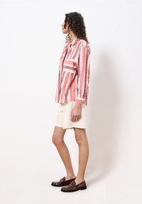 Gestreiftes Hemd in Rot und Weiß, aus leichtem Stoff, mit durchgehender Knopfleiste und Brusttasche. Kombiniert mit cremfarbenen Shorts und braunen Mokassins.