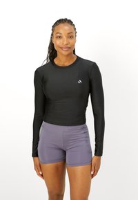 Sort langærmet atletisk top med en glat overflade og tætsiddende design, parret med lyse lilla shorts med subtile syninger.