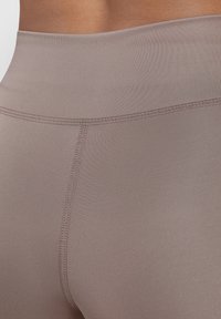 Leggings a vita alta in tessuto taupe chiaro, con una texture liscia, dettagli di cucitura e un design aderente.