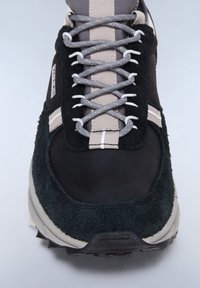 Sneaker nero e verde scuro con tomaia in pelle e suede testurizzati, lacci grigi e una suola bianca chunky con strisce di accento.