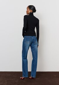 Fekete bordázott garbó pulóver, amelyet magas derekú kék egyenes szárú farmerral párosítanak. Megjegyzés: piros magassarkú cipő és arany fülbevalók.