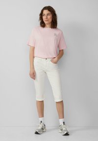 T-shirt en coton rose clair avec des manches courtes et un petit graphique, associé à un pantalon blanc coupé et des chaussures de sport argentées.