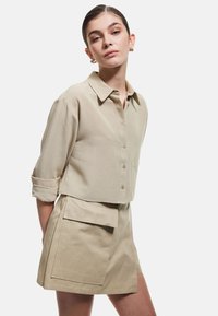 Klapet beige bluse med knaplukning foran, skjortekrave og optrukne ærmer, parret med matchende højtaljede shorts med en lomme.