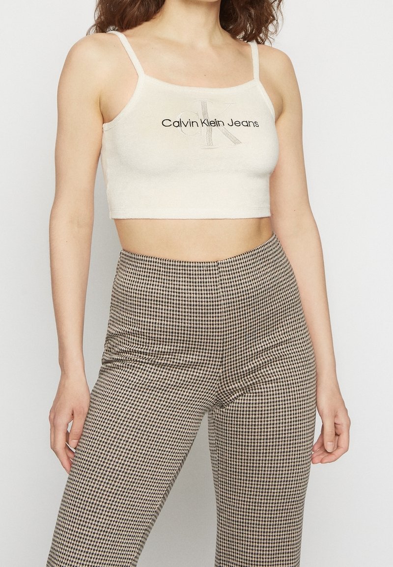 Béžový crop top s černým logem Calvin Klein, kombinovaný s kalhotami s vysokým pasem v hnědo-krémovém kostkovaném vzoru a hladkou texturou.
