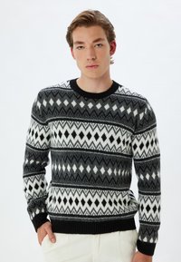 Suéter de punto en negro, blanco y gris. Presenta patrones de diamantes y triángulos, cuello redondo y puños y dobladillo acanalados.