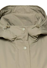 Beżowa kurtka przeciwdeszczowa z kapturem wyposażonym w regulowane sznurki i zatrzaski, ukazująca szczegółowe przeszycia i strukturę tkaniny.