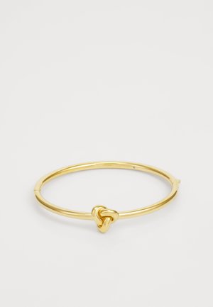 Gold-plated bangle bracelet with a smooth, circular shape and a distinctive knot design at the center. Minimalist and sleek appearance.