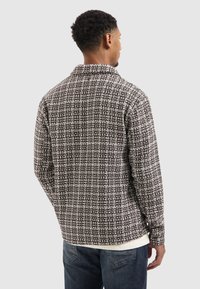 Bruin en wit geruite overhemd met lange mouwen en een kraag. Gelaagd stof, rechte zoom en knoopmanchetten. Zichtbare laag over een wit shirt.