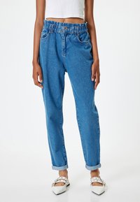 Jeans de mezclilla azul con cinturilla elástica, cinco bolsillos y puños enrollados. La tela tiene una textura deslavada y un corte relajado.