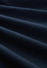 Donker marineblauwe stof met zichtbare textuurplooien die een zachte, golvende patroon creëren. De aandacht is gericht op het oppervlak van het materiaal.