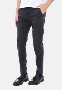 Jeans in denim nero con un taglio dritto, dotati di tasche frontali, chiusura con zip e una sottile texture. Abbinati a scarpe slip-on nere.