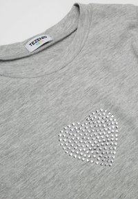 Graues Baumwoll-T-Shirt mit einem strukturierten Herzdesign aus silbernen Nieten auf der Vorderseite. Rundhalsausschnitt mit weicher Verarbeitung.