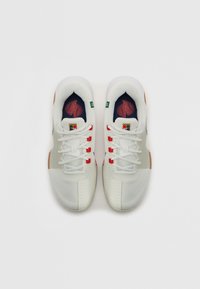 Baskets de sport blanches avec une tige en mesh, présentant des accents rouges, une semelle intermédiaire texturée et une semelle extérieure en caoutchouc marron contrastante.