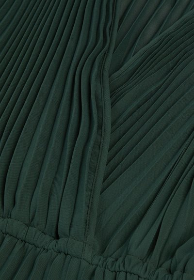 Ciemnozielona pleciona tkanina o fakturowanej powierzchni, z marszczonymi sekcjami w talii i gładkimi fałdami tworzącymi swobodny fason.