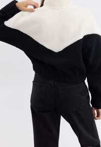 Pulóver en bloque de color blanco y negro con cuello alto, hecho de material aterciopelado, con un ajuste corto y detalle de ribete en el dobladillo.