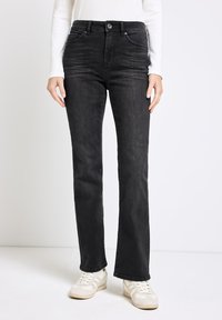 Jeans in denim nero con taglio dritto, dotati di tasche frontali, chiusura con bottone e una leggera trama scolorita. Abbinati a sneakers di colore chiaro.